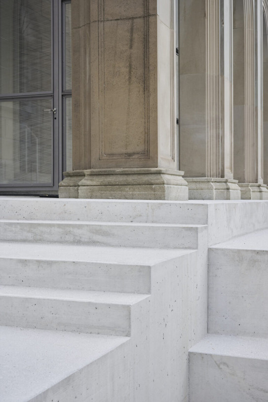 Foto von weißen Treppenstufen mit naturfarbenen Säulen und einer gläsernen Eingangstür auf dem Plateau