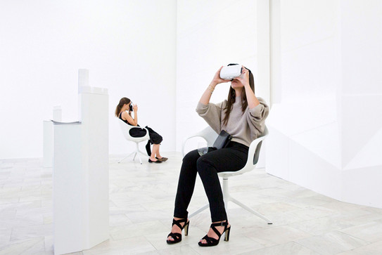2 Frauen sitzen in einem weißen Raum auf weißen Stühlen und betrachten eine digitale Ausstellung durch ein virtual Reality Gerät