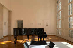 Foto eines dunklen Pianos in einem Raum mit großen Fenstern