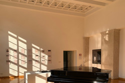 Foto eines dunklen Pianos in einem Raum mit großen Fenstern